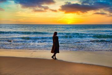 Naklejka premium a young girl stands on the shore and looks at the sea at sunset