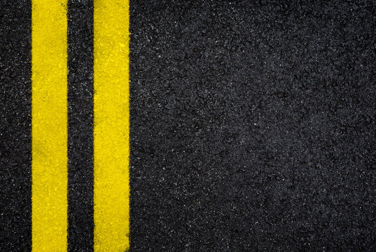 Top view of dark wet asphalt road with double yellow line. High resolution full frame textured background of black asphalt, viewed from above. Copy space.