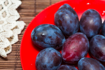 Large fresh purple plum fruits with a woven napkin on a bamboo mat, still life, close-up