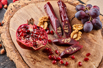 slicing Churchkhela, pomegranate, grapes and nuts on a wooden background, top view, serving