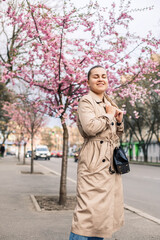 Obraz premium Beautiful woman near sakura trees. Pink flowers bloom in the trees on a city street. Trees bloom around. Spring time concept