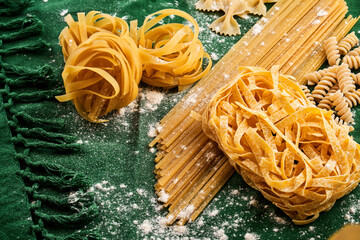 Mix of different varieties of pasta on green fabric background, cooking assorted macaroni concept