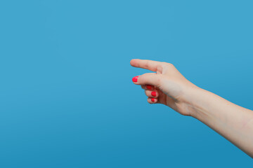 The doing woman points her finger at something. Female hand with red gel polish manicure on a blue background. Copy space
