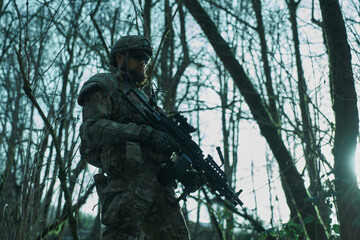 Portrait of airsoft player in professional equipment with machine gun in the forest. Soldier with weapons at war