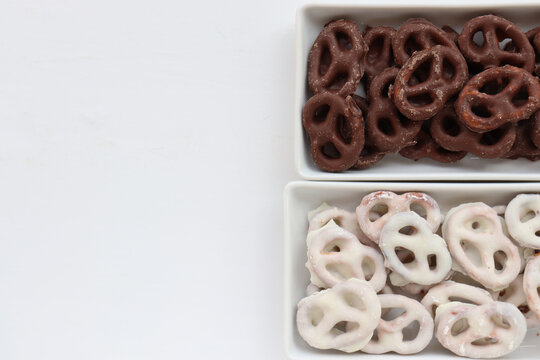 White and dark salted chocolate covered mini pretzels in a bowl on table. Homemade assorted mini pretzel chip cookies on plates on white background. Top view, copy space
