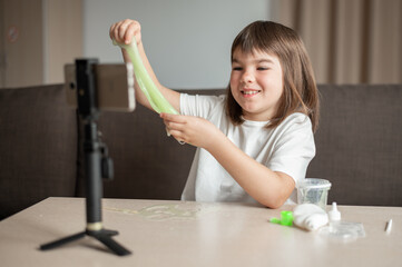 child girl 8 years old schoolgirl blogger making slime broadcasts via phone at home. High quality photo