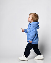 toddler in a warm blue hoodie and wide sweatpants walks to the side and shows something