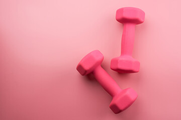 Two pink female dumbbells isolated on pink background close-up with copy space. Fitness concept, weight loss and sport activity, top view, flat lay