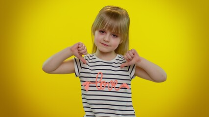 Portrait of upset blonde child girl 5-6 years old in t-shirt showing thumbs down sign gesture,...