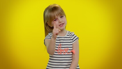 Blonde kid child 5-6 years old shakes finger and saying no, be careful, scolding and giving advice to avoid danger mistake, disapproval sign. Yellow studio background. Teenager children girl emotions