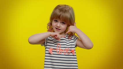 Portrait of funny playful blonde child girl 5-6 years old in striped t-shirt looking at camera doing phone gesture like says hey you call me back on yellow studio wall background. Teen kid children