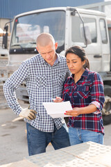 Couple of wokers, man and woman, checking order list at hardware store warehouse