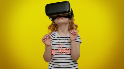 Little teen child kid girl using virtual reality futuristic technology VR app headset helmet to play simulation 3D 360 video game, drawing. Young children posing isolated on yellow studio background