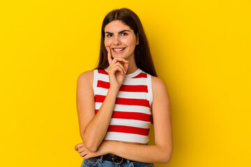 Young caucasian woman isolated on yellow background smiling happy and confident, touching chin with hand.