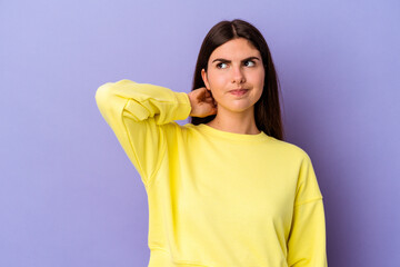 Young caucasian woman isolated on purple background touching back of head, thinking and making a...
