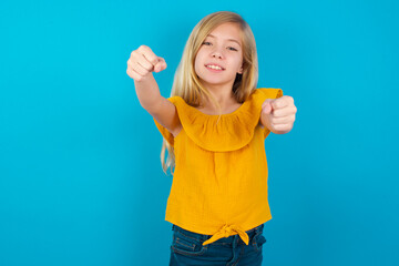 Caucasian kid girl wearing yellow T-shirt against blue wall imagine steering wheel helm rudder...