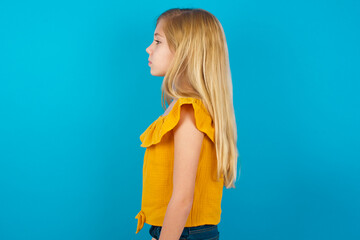 Caucasian kid girl wearing yellow T-shirt against blue wall looking to side, relax profile pose...