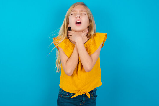 Caucasian kid girl wearing yellow T-shirt against blue wall shouting suffocate because painful strangle. Health problem. Asphyxiate and suicide concept.