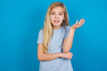 Fototapeta premium Studio shot of frustrated beautiful Caucasian little girl wearing blue T-shirt over blue background gesturing with raised palm, frowning, being displeased and confused with dumb question.