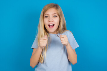 Portrait of desperate and shocked beautiful Caucasian little girl wearing blue T-shirt over blue background looking panic, holding hands near face, with mouth wide open.