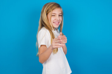 Hey you, bang. Joyful and charismatic good-looking beautiful Caucasian little girl wearing white T-shirt over blue background winking and pointing with finger pistols at camera happily and cheeky.