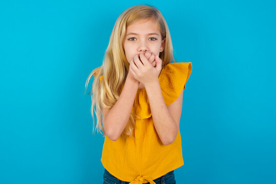 Caucasian Kid Girl Wearing Yellow T-shirt Against Blue Wall Holding Oneself, Feels Very Cold Outside, Hopes That Will Not Get Cold