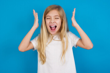 beautiful Caucasian little girl wearing white T-shirt over blue background goes crazy as head goes around feels stressed because of horrible situation