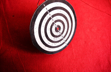 Used dart board standing on red carpet and its shadows.