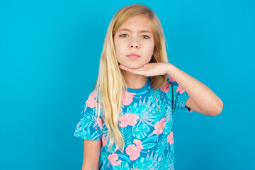 Caucasian kid girl wearing hawaiian T-shirt against blue wall cutting throat with hand as knife,...