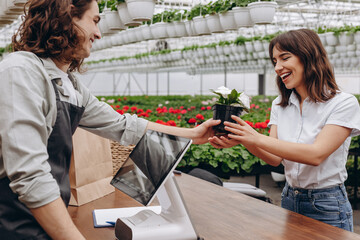 Photo of young woman buy flowerpot with florist man in greenhouse garden center.