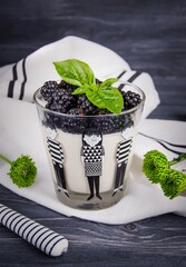 Traditional italian dessert panna cotta with fresh blackberries and green basil on a dark wooden background