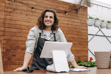 Attractive male florist and standing near cash register, waiting for clients in flower shop.