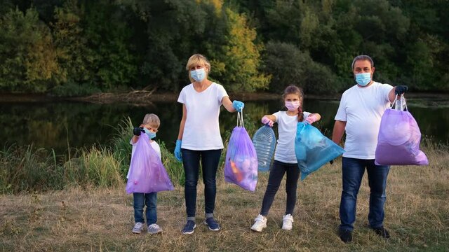 A family of volunteers posing with blue plastic bags and showing big like after they finish to collecting the plastic bags. Environment, ecology, biosphere protection concept..