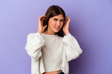 Young caucasian woman isolated on purple background covering ears with fingers, stressed and...