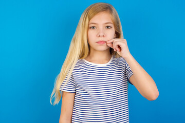 Caucasian kid girl wearing striped shirt ​against blue wall  mouth and lips shut as zip with...