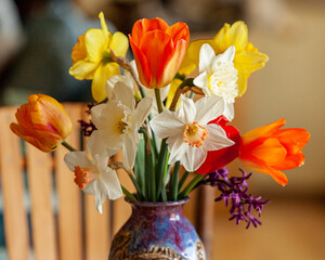 A bright spring bouquet of daffodils and tulips in a purple vase on a table.