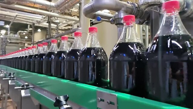 Dark liquid sweet soft drink moving at conveyor footage