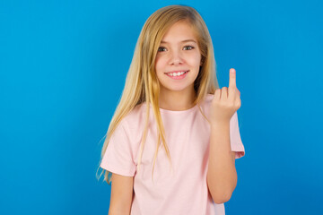 Caucasian kid girl wearing pink shirt against blue wall shows middle finger bad sign asks not to...
