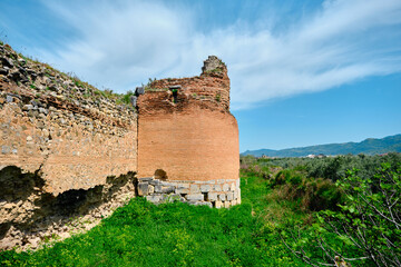 Old and ancient city wall in nicaea (iznik Bursa) established by Byzantium with ruin and stones graves with many green grass and yellow flowers during sunny day and small pathway along the huge grass.