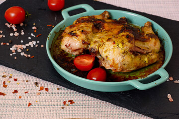 Grilled chicken with tomatoes. Roasted chicken in a blue ceramic baking sheet, on a black tray - 431810468