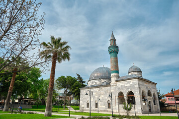Fototapeta na wymiar 29.4.2021. Bursa, Turkey. Green mosque (yesil camii) in Nicaea (iznik) during spring and sunny day in center of the city covered by many green plants, and palm trees and it turquoise color minaret