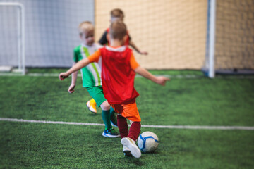 Football soccer game for kids, junior young football team group of children team having training session, or football game on a pitch, running and kicking ball on green pitch