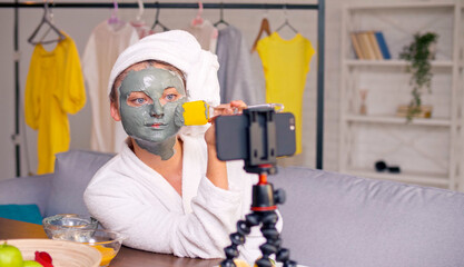 A Beauty Blogger in a White Robe with a White Towel on Her Head Applies a Green Moisturizing Mask to Her Face and Blogs about Skin Care and Cosmetics. Next Generation of Beauty Influencers