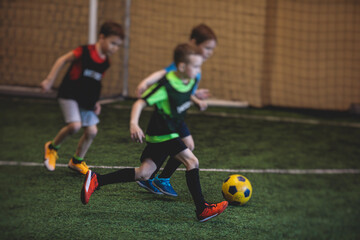 Football soccer game for kids, junior young football team group of children team having training session, or football game on a pitch, running and kicking ball on green pitch
