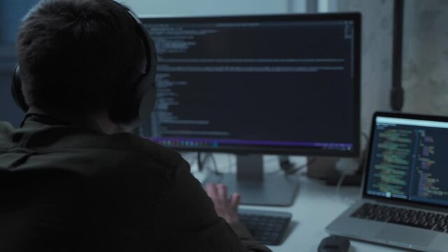 Programmer in headphones cancel noise working on new software development behind computer and laptop. Application developer working on computer in office. Work from home, remote working concept