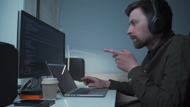 Concept of smartworking in lockdown. Man programmer in headphones sitting at at computer workplace at home office . Coding, programming. Software engineer working on programming code for new project
