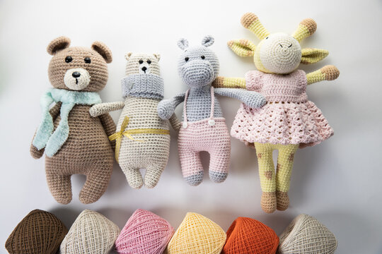 Soft bright dolls made of yarn lie on a white background with balls of multi-colored yarn. Needlework, agourami