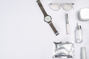 trendy stylish flat lay in silver colour: eye patches, glasses for vision, wrist watch, cream, serum, mascara on a white background