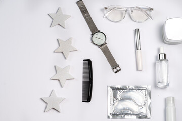 trendy stylish flat lay in silver colour: eye patches, glasses for vision, wrist watch, cream, serum, mascara on a white background