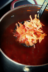 Hot vegetable tomato soup borscht in a saucepan. A ladle is stirring borscht in a saucepan.